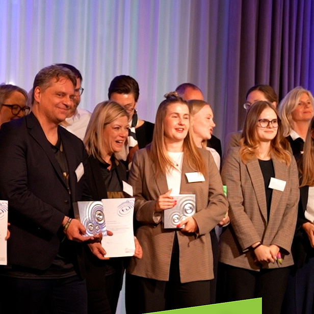 Eine Gruppenaufnahme von Menschen, die einen Preis zum InnoWard Bildungspreis erhalten. Im Vordergrund hält eine Person eine Urkunde. Ein grünes Banner informiert über die Bewerbung für den Preis bis zum 31. Mai 2026.